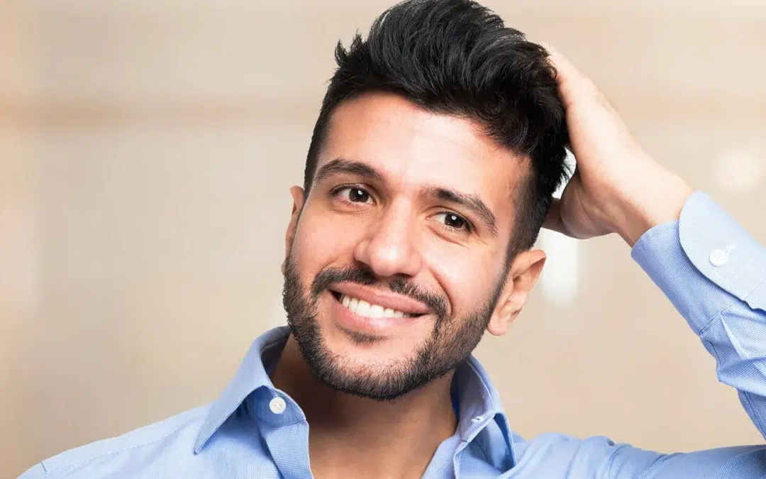 Smiling man in a blue dress shirt touching his thick, styled dark hair.